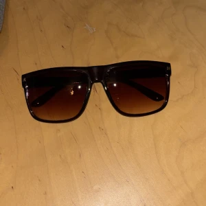 Helt nya Bruna solglasögon - Helt nya Stilrena solglasögon med fyrkantig form och bruna bågar i plast. Glasen är tonade i brunt och ger en modern look. Perfekta för att lyfta din outfit med en trendig accessoar.