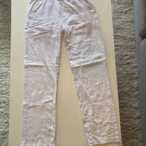 Vita linnebyxor med resårmidja - Säljer ett par vita linnebyxor med resår i midjan och raka ben. Byxorna har fickor fram och en bakficka. Perfekta för varma dagar och har en avslappnad passform. De är små i storleken och passar inte mig som är 159