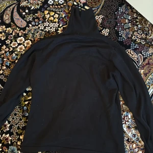 Svart tröja med ribbade ärmslut - En svart tröja med långa ärmar och ribbade muddar vid ärmsluten. Enkel och stilren design som passar till många olika outfits.