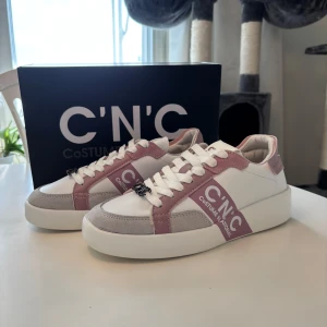 Sneakers  - Snygga vita sneakers med rosa och grå detaljer från C'N'C Costume National i storlek 38. Skorna är helt oanvända och skickas i original kartong. Skriv om du har några funderingar, pris kan diskuteras!