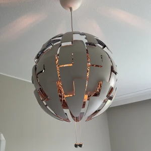 Vit taklampa  - Bilderna visar en modern taklampa med ett unikt, sfäriskt och futuristiskt designmönster. Lampan har vita och silvriga segment som kan öppnas och stängas, vilket skapar en cool ljuseffekt. Perfekt för dig som vill ha en iögonfallande inredningsdetalj i ditt rum.