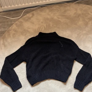 Svart stickad croppad tröja från Divided H&M - Säljer en svart stickad croppad tröja från Divided H&M. Tröjan har lång ärm, ribbade muddar och hög hals. Perfekt för lager-på-lager och enkel att matcha med jeans eller kjol. Hör av dig vid intresse eller frågor❤️
