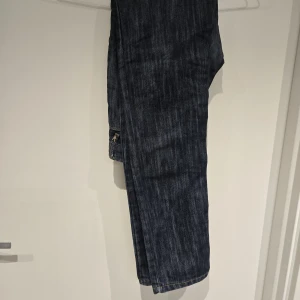 Playboy jeans med strassdetalj - Mörkblå jeans från Playboy med raka ben och snygga kontrastsömmar. Bakfickorna är klassiska och framtill finns en unik knapp med Playboy-loggan dekorerad med strass. Jeansen är tillverkade i 100% bomull och har en normal passform. Massa fina detaljer på dessa jeans!