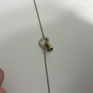 Edblad armband - Snyggt armband i guldfärg med ett hjärta dekorerat med små glittriga stenar och en rund guldfärgad detalj. Tunt kedjeband som ger en stilren look. Perfekt accessoar för att lyfta din outfit.