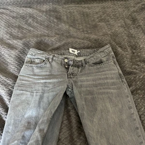 Grå jeansbyxor från 157 - Säljer ett par grå jeansbyxor från 157 med klassisk femficksdesign och raka ben. Byxorna har låg midja och stängs med dragkedja och knapp. Perfekta för en avslappnad stil.