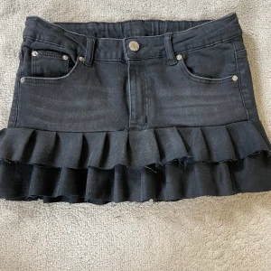 Svart jeanskjol med volang - Egensydd jenaskjol som är svart.  Midjemåttet är 36cm men tyget är väldigt stretchigt så den ska nog passa upp till 39cm. Inneti finns resårband så att man kan göra den mindre än 36cm.