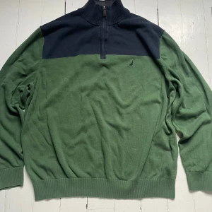 Grön och marinblå tröja med halv dragkedja från Nautica - Säljer en grön tröja med marinblå axelparti och hög krage med halv dragkedja från Nautica. Tröjan har långa ärmar och ribbade muddar vid ärmslut och nederkant. Liten broderad logga på bröstet.