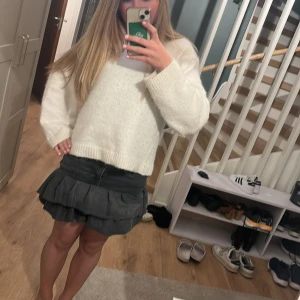 Svart volangkjol i jeans - Säljer en svart kort jeanskjol med volanger. Kjolen har klassisk jeansmidja med knapp och dragkedja samt två lager volanger som ger en cool och trendig look.