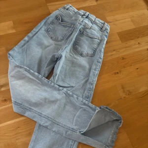 Ljusblå jeansbyxor från Gina Tricot - Säljer ett par ljusblå jeansbyxor från Gina Tricot med klassisk femficksdesign och hög midja. Jeansen har raka ben och en slits nertill. Perfekta till vardags och lätta att matcha med olika toppar. OBS! Byxorna är insydda och har midjemått 28 från höft till höft!