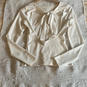 Vit ribbad långärmad topp med knyt - Säljer en vit ribbad långärmad topp med snygg knytning baktill. Toppen har en smickrande passform och är tillverkad i ett mjukt material som känns skönt mot huden. Perfekt att styla med jeans eller kjol. Storlek är oklar men skulle säga xs/s men den har också stretch så funkar som en M om man vill 
