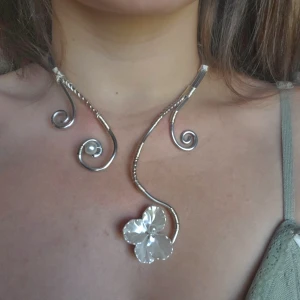 Handgjord Silvrigt halsband med blomma och pärldetalj - Unikt handgjort adjustable halsband i silverfärgad metall med snirkliga detaljer🤍 Halsbandet har en stor, skimrande blomma och en vit pärla som dekoration. Pris inkluderar material och tid det tog att tillverka. Silver rostar inte! 