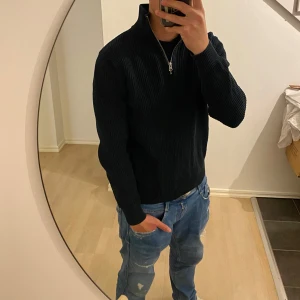 Svart ribbad halvzip tröja - Säljer en svart ribbad tröja med halv dragkedja i halsen. Tröjan har lång ärm och hög krage, perfekt för lager-på-lager. Passar till både jeans och andra byxor för en stilren look.