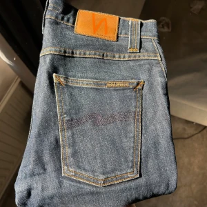 Mörkblå jeans från Nudie Jeans - Säljer ett par klassiska mörkblå jeans från Nudie Jeans med orange sömmar och läderpatch bak. Modellen har raka ben och fem fickor. Perfekta för dig som gillar stilrena och tidlösa jeans.
