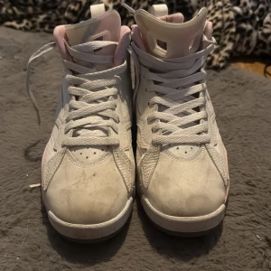 Nike Air Jordan sneakers i vitt och rosa - Säljer ett par Nike Air Jordan sneakers i vitt med ljusrosa detaljer. Skorna har högt skaft, snörning och klassisk Jordan-logga på sidan. Perfekta för dig som gillar streetwear och vill sticka ut med en snygg färgkombo.