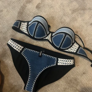 Blå och svart bikini från Triangel - Säljer en snygg bikini från Triangel i blått och svart med vita dekorativa sömmar. Jätte fin och perfekt inför sommaren. Väldigt populär och svår att få tag på! Överdel storlek Large, nederdel storlek Large.