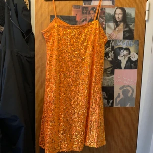 Orange paljettklänning med smala axelband - Säljer en glittrig orange klänning med smala axelband och rak passform. Klänningen är täckt av paljetter som ger en riktigt festlig look. Perfekt för dig som vill sticka ut och glänsa på nästa fest!