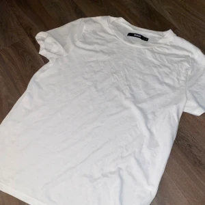 Vit basic t-shirt från bikbok  - En klassisk vit t-shirt från bikbok med rund halsringning och normal passform. Perfekt basplagg i mjuk bomull som funkar till allt. Kortärmad och enkel design utan tryck eller detaljer.