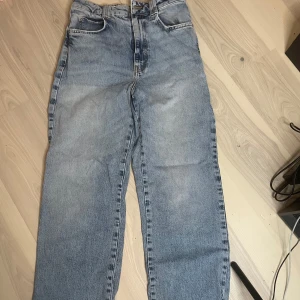 Blå raka jeans från Zara - Säljer ett par klassiska blå jeans från Zara med rak passform och hög midja. Jeansen har 4 fickor och stängs med dragkedja och knapp. Perfekta till vardags för en avslappnad stil.
