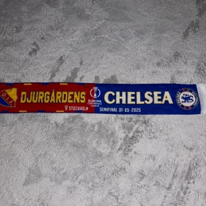 Djurgårdens IF vs Chelsea halsduk Europa League - Säljer en halsduk från Europa League-semifinalen mellan Djurgårdens IF och Chelsea, spelad i Stockholm 2025. Halsduken har Djurgårdens och Chelseas loggor samt text i gult, blått och rött. Perfekt för samlare eller fans!