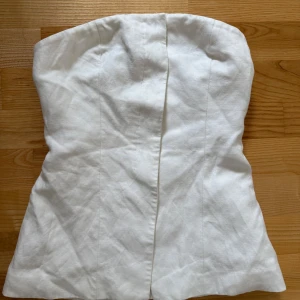 Vit tubtopp från H&M i linnemix - Säljer en stilren vit tubtopp från H&M i linnematerial. Toppen är axelbandslös och har en slits-detalj framtill. Perfekt att matcha med jeans eller kjol för en fräsch look.