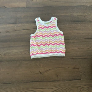 Stickad ärmlös topp med vågmönster från Lindex - Superfin stickad topp från Lindex med vågigt mönster i rosa, grön, gul och vit. Ärmlös modell med ribbad kant vid hals och ärmhål. Perfekt för varma dagar och enkel att matcha med jeans eller kjol.