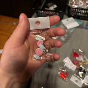 Pastellfärgade örhängen med godisdesign - Säljer ett par söta örhängen formade som godisklubbor i pastellfärger, med rosa och blå snurrmönster och ljusblå rosetter. Perfekta för dig som gillar lekfulla accessoarer!