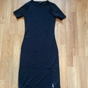Svart ribbad klänning från Gina Tricot - Säljer en svart ribbad klänning från Gina Tricot i storlek S. Klänningen har korta ärmar, rund halsringning och en liten slits nertill. Modellen är kroppsnära och i mjukt stretchigt material, perfekt för en stilren look.