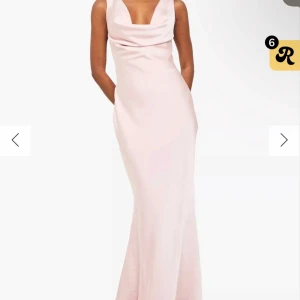 Ljusrosa långklänning med öppen rygg och snörning - Elegant ljusrosa långklänning med draperad urringning och öppen rygg med snygg snörningsdetalj. Klänningen har en figurnära passform och är tillverkad i ett glansigt, slätt material som ger en lyxig känsla.