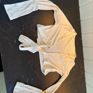 Beige ribbad omlottopp - Säljer en beige ribbad omlottopp med långa ärmar och knytband i midjan. Toppen har ett mjukt och stretchigt material och passar perfekt till både jeans och kjol. Enkel men ändå trendig design.