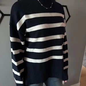 Mörkblå och vit randig stickad tröja - Säljer en mörkblå stickad tröja med breda vita ränder. Tröjan har lång ärm, rund hals och ribbade muddar vid ärmslut och nederkant. Perfekt för en avslappnad och stilren look.