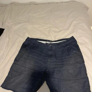 Mörkblå linne shorts från Bruun & Stengade - Nypris 800kr!!!! Snygga mörkblå shorts från Bruun & Stengade med klassisk passform. Shortsen har knapp och dragkedja framtill samt två bakfickor med diskret metallogo. Perfekta för sommardagar och stilrena outfits.