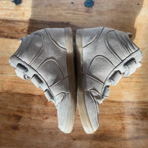 Beige sneakers med kardborreband - Säljer ett par beige sneakers med högt skaft och tre breda kardborreband. Skorna har en rund tå och är gjorda i mocka med en ljusbrun sula. Perfekta för dig som vill ha en stilren och bekväm sko med lite extra höjd.