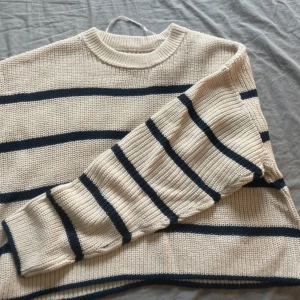 Beige stickad tröja med marinblå ränder från ONLY - Säljer en beige stickad tröja från ONLY med marinblå horisontella ränder. Tröjan har rund halsringning och långa ärmar. Perfekt för lager-på-lager och enkel att matcha med jeans eller kjol.