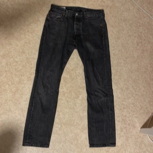 Svarta Levi's 501 jeans W30 L30 - Klassiska svarta Levi's 501 jeans med raka ben och femficksdesign. Jeansen har knappgylf och den ikoniska läderpatchen bak i midjan. Perfekta för dig som gillar tidlös stil och vill ha ett par jeans som funkar till allt.