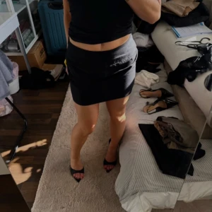 Svart kortkjol i bomull - Enkel och stilren svart kortkjol i bomull med tight passform. Kjolen har en diskret dragkedja i sidan och är perfekt att matcha med crop tops eller t-shirts. Klassisk design utan mönster eller extra detaljer.