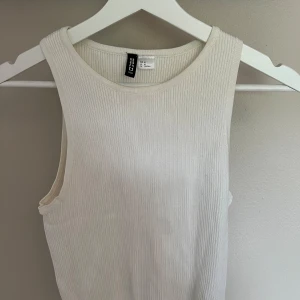 Vit ribbad linnetopp från H&M - Säljer en enkel och stilren vit ribbad linnetopp från H&M. Toppen är ärmlös med rund halsringning och tillverkad i ett mjukt, stretchigt material. Perfekt att matcha med jeans eller kjol.