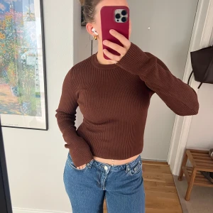 Brun ribbad tröja från NA-KD - Säljer en brun ribbad långärmad tröja från NA-KD. Tröjan är croppad och har en rund halsringning. Perfekt att matcha med jeans eller kjol för en snygg vardagslook.