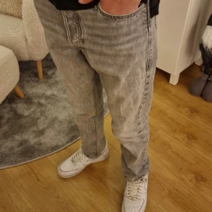 Grå jeans från Jack & Jones - Säljer ett par grå loose jeans från Jack & Jones med klassisk femficksdesign och knappgylf. Byxorna har en loose fit och raka ben, perfekt för en avslappnad stil. Snygga detaljer och slitna kanter nertill för en trendig look. Lite små fläckar på benen och uppdraget tyg längst ner. Ny pris 699.