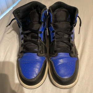 Nike Air Jordans 1 mid  - Säljer ett par klassiska Nike Air Jordan 1s mid (gs) hyper royal läder, och vit sula. Skorna har svart snörning och den ikoniska Air Jordan-loggan på sidan. Perfekta för dig som gillar streetwear och sneakers med attityd.