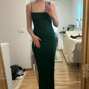 Mörkgrön långklänning med slits - Säljer en mörkgrön långklänning i silkesmaterial med slits. Jag är själv 180cm så slitsen blir väldigt hög, på någon kortare blir den lägre. Köptes i Albanien för 1000kr men är helt oanvänd med lappen kvar! Perfekt som klänning till balen!