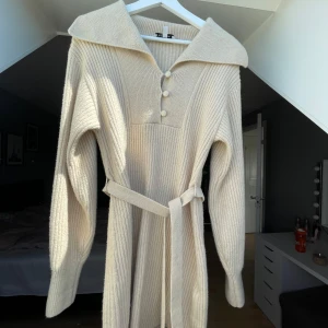 Beige stickad klänning från & Other Stories - Superfin beige stickad klänning från & Other Stories med stora krage, knappar framtill och knytskärp i midjan. Långärmad och ribbad, perfekt under kallare dagar.