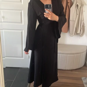 Svart omlottklänning med lång ärm - Säljer en svart omlottklänning med långa ärmar och knyt i midjan. Klänningen har en v-ringad hals och är i en elegant, flowy modell som ger en snygg siluett. Stor i storleken, så skulle säga att de är mer än 36