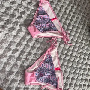 2st Rosa bikiniöverdelar från Victoria's Secret - Säljer två rosa bikiniöverdel från Victoria's Secret med broderade mönster i blått, lila och svart. Triangelformad modell med knyt i nacken och ryggen. Perfekt för stranden eller poolen! Båda tillsammans för 100kr -enskilt 50 kr
