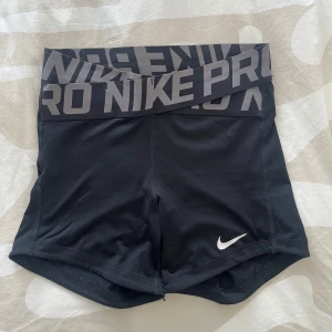 Svarta Nike Pro Dri-FIT shorts - Svarta träningstights-shorts från Nike Pro med bred resår i midjan och grå logga. Tillverkade i stretchigt Dri-FIT material som andas. Perfekta för intensiva träningspass eller sport.