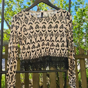 Svartvit mönstrad croppad tröja med fransar - Säljer en croppad långärmad tröja i svartvitt mönster med snygga fransdetaljer nertill. Tröjan har rund halsringning och är perfekt för dig som vill sticka ut lite extra.