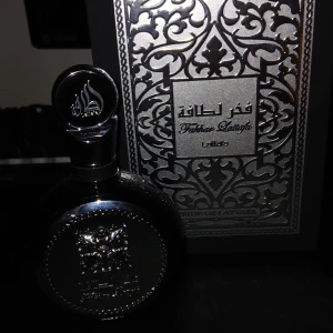 Fakhar Lattafa Pride Eau de Parfum - Exklusiv parfym från Lattafa med elegant svart och silverfärgad flaska och dekorativt mönster. Flaskan har rund form och metallisk finish med arabiska inskriptioner och detaljerad emblem på framsidan. Kommer i lyxig ask med matchande design. Är öppnade och testad runt 5 sprej