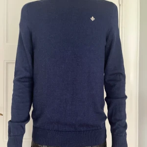 Mörkblå stickad morriströja  - Mörkblå stickad tröja från Morris med liten broderad logga på bröstet. Klassisk modell med rund hals och ribbade muddar vid ärmslut och nederkant. Perfekt till både jeans och chinos. Den har ett litet hål på ryggen(bild 3). Stl M men sitter som S. Hör av er vid frågor eller funderingar!