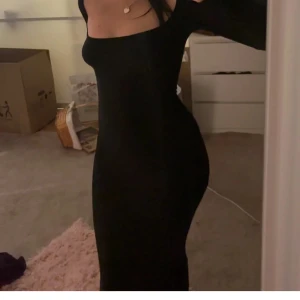 SKIMS Svart långklänning med lång ärm och fyrkantig ringning - Säljer en elegant svart långklänning med tight passform och lång ärm. Klänningen har en snygg fyrkantig ringning och är figurnära hela vägen ner. Perfekt för dig som vill ha en stilren och klassisk look. Köpt från skims och knappt använd 