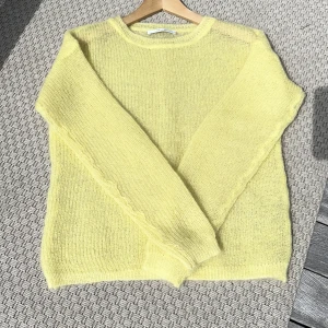 Ljusgul stickad tröja från Gestuz - Härlig och fluffig ljusgul stickad tröja från Gestuz. Tröjan har rund halsringning och långa ärmar med ribbade muddar. Perfekt för lager-på-lager och ger en fräsch färgklick till garderoben. Storlek xs