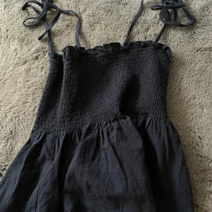 Svart smockad top  - Supersöt svart top från Shein med smockad överdel och tunna axelband som knyts på axlarna. Klänningen har en luftig kjol och är perfekt för varma dagar. Materialet känns lätt och bekvämt mot huden.